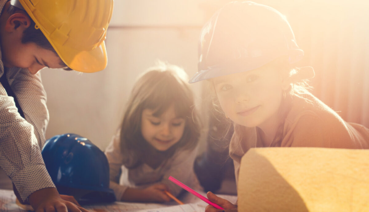 Kinder mit Bauhelm zeichnen einen Bauplan