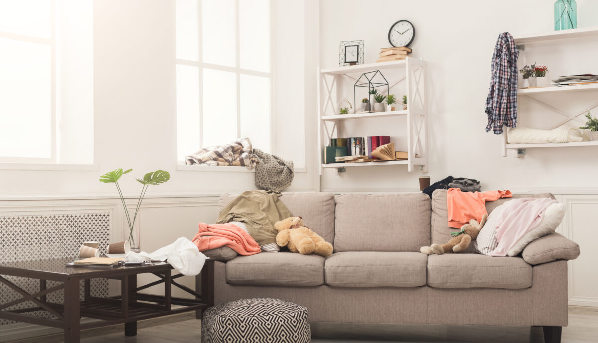Unordentliches Wohnzimmer mit Kleidern auf dem Sofa